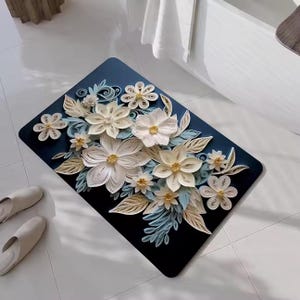 May include: A rectangular navy blue bath mat featuring a floral design. The flowers are crafted from paper in shades of white, cream, and light blue. The mat is placed on a white tiled floor, with a pair of cream-colored slippers nearby.