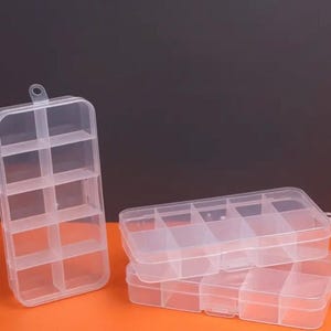 Puede incluir: Tres cajas de almacenamiento de plástico transparente con múltiples compartimentos. Las cajas están apiladas una encima de la otra. La caja superior tiene seis compartimentos, la caja del medio tiene seis compartimentos y la caja inferior tiene nueve compartimentos.