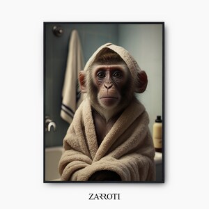 Op de afbeelding: Een bruine aap die een beige badjas draagt met de capuchon omhoog, kijkt recht in de camera. De aap zit in een badkamer met een handdoek die aan de muur achter hem hangt.