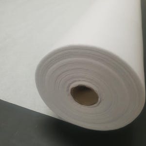 Może przedstawiać: Biała rolka flizeliny, rodzaj materiału termotopliwego stosowanego w projektach szycia i patchworku.