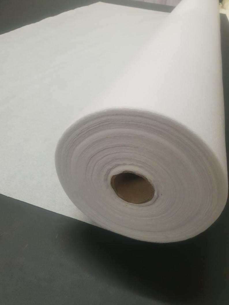 Może przedstawiać: Biała rolka flizeliny, rodzaj materiału termotopliwego stosowanego w projektach szycia i patchworku.
