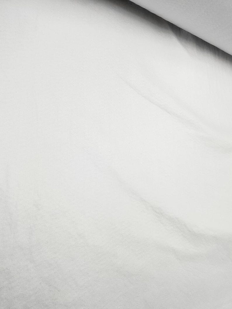K&ouml;nnte beinhalten: Wei&szlig;er Stoff mit glatter Textur. Der Stoff ist gefaltet und hat eine leichte Falte.