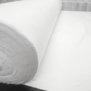 May include: A white roll of fabric, unfurled to reveal the soft, white material. The fabric is tightly wound and appears to be a type of non-woven material.