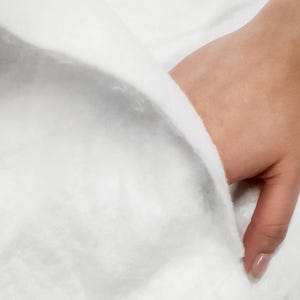 K&ouml;nnte beinhalten: Nahaufnahme eines wei&szlig;en, flauschigen Stoffes mit einer Hand, die den Rand des Stoffes h&auml;lt.
