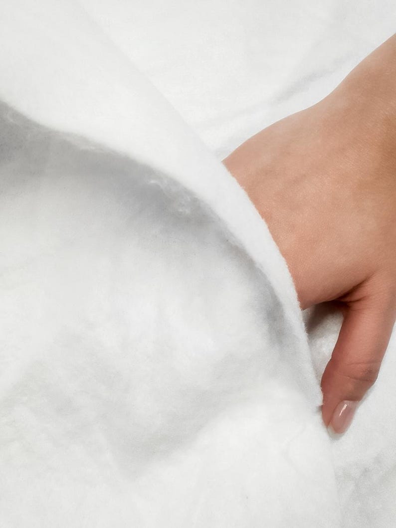 K&ouml;nnte beinhalten: Nahaufnahme eines wei&szlig;en, flauschigen Stoffes mit einer Hand, die den Rand des Stoffes h&auml;lt.