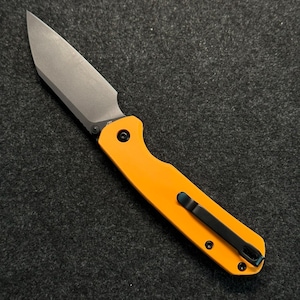 May include: A yellow pocket knife with a black handle and a silver blade. The knife has a pocket clip and a safety lock.