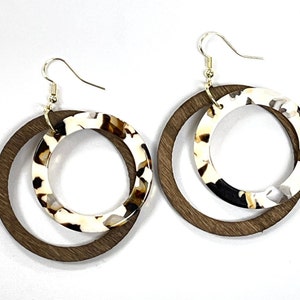 May include: A pair of brown wood and white and brown patterned resin hoop earrings. The earrings are double layered with the wood hoop on the outside and the resin hoop on the inside.