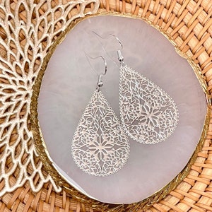 May include: A pair of silver teardrop-shaped earrings with a delicate filigree design.