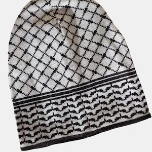 May include: A white and black knitted beanie hat. The hat has a repeating diamond pattern across the crown. The brim has a black zig-zag design with a black band above it. The hat is made of a soft, knitted material.