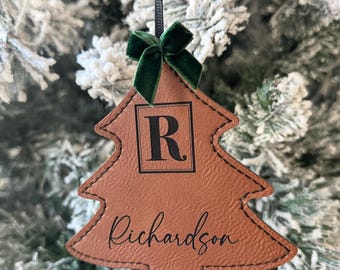 May include: A brown leather Christmas tree ornament with a green velvet bow. The ornament is personalized with the letter "R" and the name "Richardson".