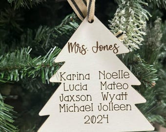 May include: A wooden Christmas tree ornament with the name "Mrs. Jones" and family names, including "Karina," "Noelle," "Lucia," "Mateo," "Jaxson," "Wyatt," "Michael," and "Jolleen." The year "2024" is also inscribed. The ornament hangs from a striped ribbon.