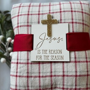 May include: A red and white checked blanket with a gold glitter cross and a sign that reads "Jesus is the reason for the season".