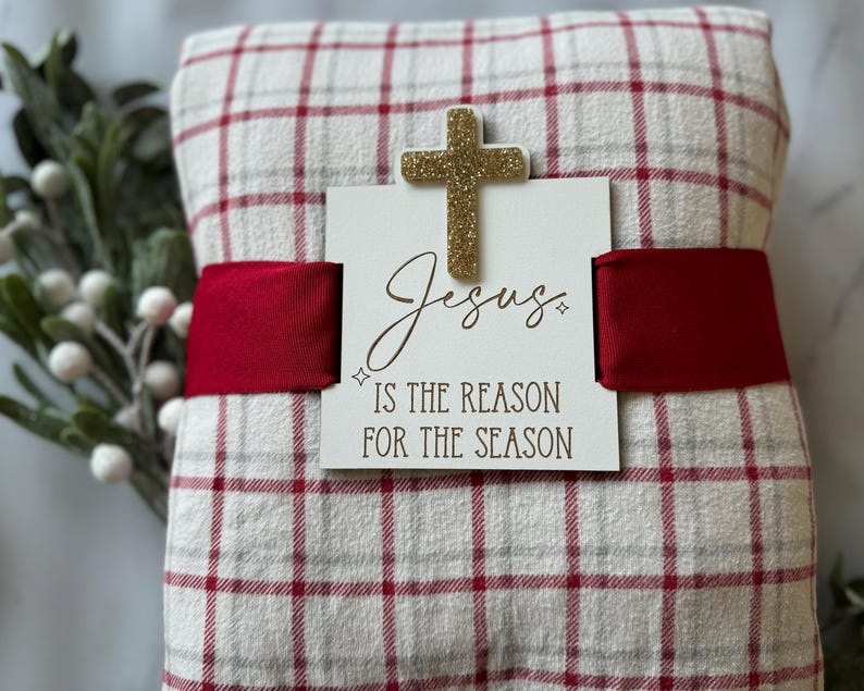 May include: A red and white checked blanket with a gold glitter cross and a sign that reads "Jesus is the reason for the season".