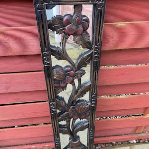 Peut inclure: Miroir rectangulaire en bois brun foncé avec un motif floral sculpté. Le miroir présente un vase en bas, avec une tige florale et des fleurs au centre. Le cadre a une bordure décorative.