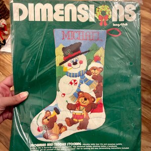 May include: A Dimensions longstitch needlepoint kit for a Christmas stocking featuring a snowman wearing a black hat and blue scarf, accompanied by three teddy bears. The packaging displays the name Michael and measures 40 cm long.