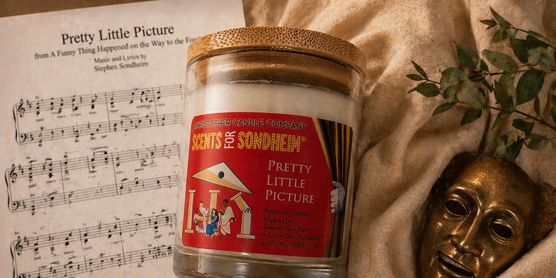 May include: A candle in a glass jar with a bamboo lid, labeled "Scents for Sondheim Pretty Little Picture." The label is red with a theater scene illustration. Sheet music and a golden theater mask are in the background.