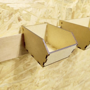 May include: Three wooden wall-mounted storage bins with a light brown finish. The bins are attached to a light wood wall.