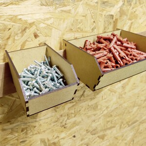 May include: Two wooden wall-mounted storage bins with dividers. The bin on the left is filled with silver screws. The bin on the right is filled with red plastic anchors.