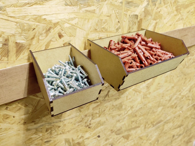 May include: Two wooden wall-mounted storage bins with dividers. The bin on the left is filled with silver screws. The bin on the right is filled with red plastic anchors.