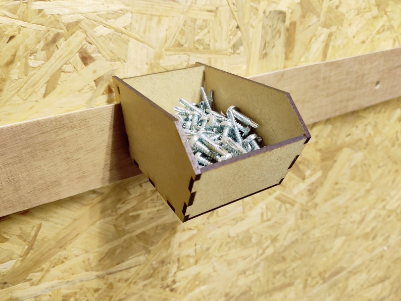 May include: A small wooden box with a lip on the front, mounted to a wall, filled with silver screws.