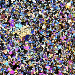 Könnte beinhalten: Eine mikroskopische Ansicht eines mineralischen Dünnschliffs mit einem dichten, granularen Mosaik aus ineinandergreifenden Kristallen in leuchtendem Magenta, Elektroblau, Goldgelb und Tiefschwarz, die ein komplexes geometrisches Muster bilden.