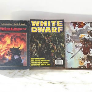May include: Three fantasy gaming magazines. The first is "Advanced Dungeons & Dragons" with a dragon illustration. The second is "White Dwarf" with a group of figures. The third has a battle scene.