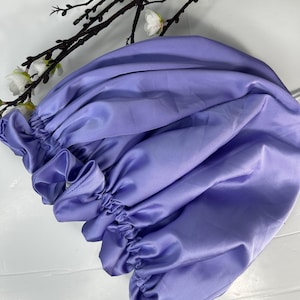 May include: A lavender satin hair bonnet with a gathered elastic band. The bonnet is made of soft, smooth fabric and is designed to protect hair from breakage and frizz.