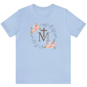May include: Light blue t-shirt with a floral wreath design featuring a cross and the letters "M" and "M".