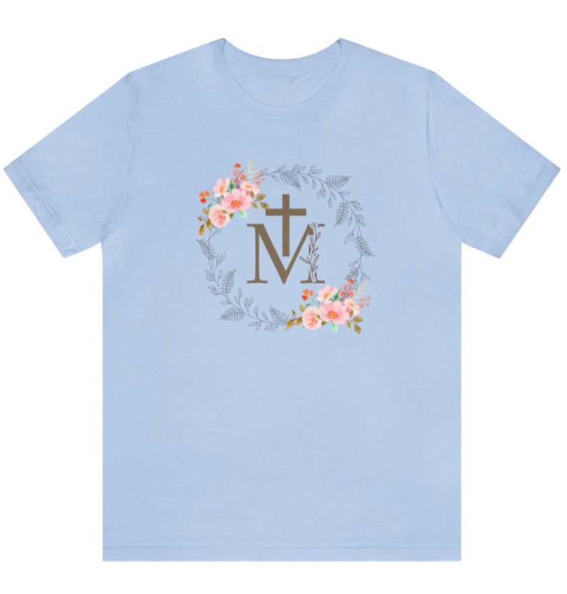 May include: Light blue t-shirt with a floral wreath design featuring a cross and the letters "M" and "M".
