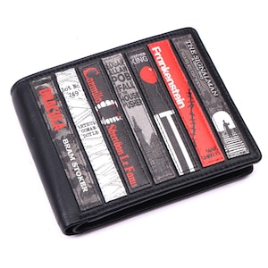 May include: Black leather wallet featuring book spine designs with titles like "Dracula," "Frankenstein," and "The Signalman." The spines are in various colors, including red, gray, and white, with author names and illustrations. The wallet has a bi-fold design.