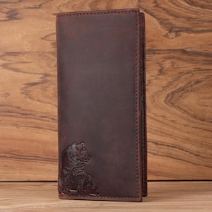 May include: A brown leather wallet with a bear embossed on the front. The wallet is vertically oriented and has a bi-fold design. The leather has a distressed appearance, and the stitching is visible along the edges. The bear is depicted in a detailed, naturalistic style.