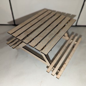 Op de afbeelding: Een miniatuur houten picknicktafel met een lattenblad en zitbanken. De tafel is gemaakt van lichtbruin hout en heeft een natuurlijke afwerking.
