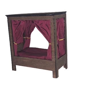 Op de afbeelding: Een houten poppenhuisbed met een bordeauxrode kap en een bordeauxrode matras.