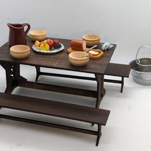 May include: A miniature wooden table set with two benches, a pitcher, bowls, and a plate of fruit. The table is brown and the benches are dark brown. There is a small white mouse figurine on the table.