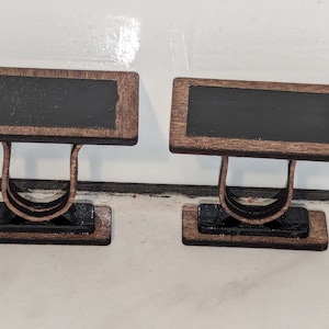 Può includere: Due lavagne in miniatura di legno con cornici marroni e basi nere. Le lavagne sono vuote e pronte per essere scritte.