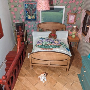 Könnte beinhalten: Eine Miniatur-Schlafzene mit einem Holzbett, einer Bettdecke mit Blumenmuster und einem kleinen Teddybären. Der Raum verfügt über eine Hundefigur, einen kleinen Tisch mit einer Lampe und ein gerahmtes Bild. Die Wände sind mit floraler Tapete dekoriert.