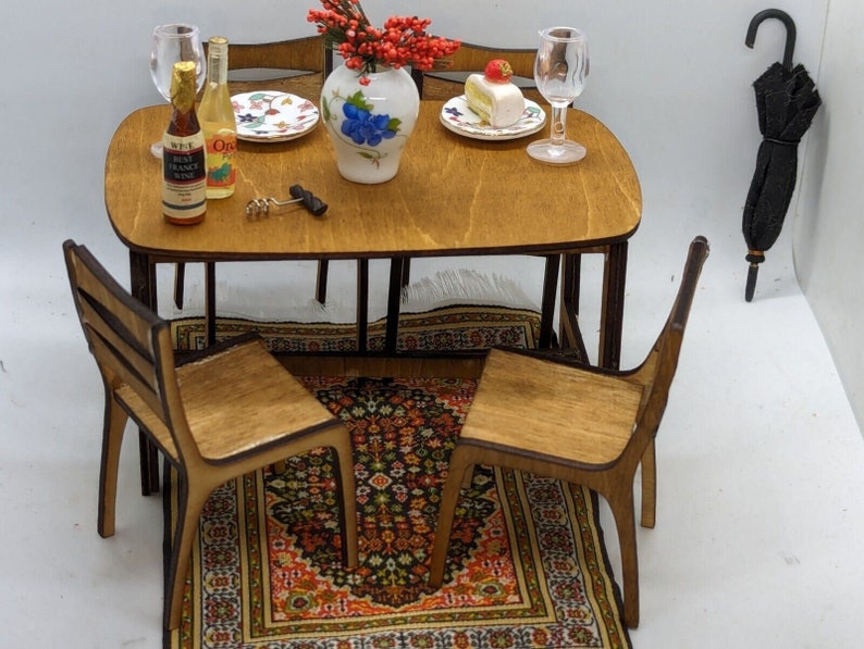May include: A miniature wooden dining set with a brown table, two chairs, and a rug. The table is set with two wine glasses, a bottle of wine, a plate with a dessert, and a vase with red flowers.