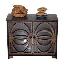 May include: A dark brown wooden cabinet with two glass doors. The doors have a decorative pattern of circles and ovals. There are two plates of bread on top of the cabinet.