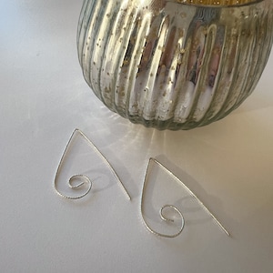 May include: A pair of silver earrings with a delicate, curved design and a spiral detail. The earrings are on a white surface.