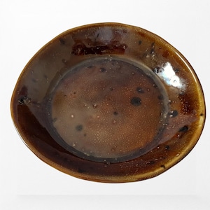 Può includere: Un piatto in ceramica marrone fatto a mano con finitura lucida. Il piatto ha una forma irregolare e organica ed è macchiato di macchie scure. Il bordo è leggermente rialzato e l'interno ha un aspetto strutturato. Adatto per servire cibo.