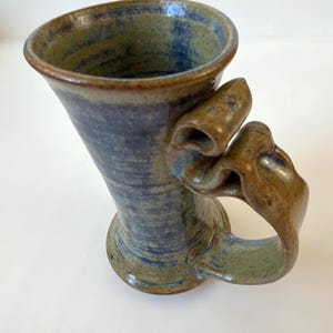 Taza de cerámica de estudio firmada, asa escultural, tonos tierra y esmalte azul. Estilo de mediados de siglo.