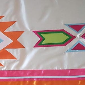 Puede incluir: Tela de satén blanca con diseños geométricos coloridos. El diseño presenta formas naranjas, blancas, rosas, azules y verdes. Una cinta rosa y naranja bordea la parte inferior de la tela. La tela tiene un aspecto brillante.
