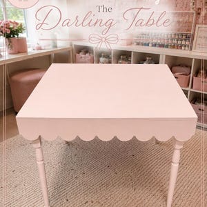 May include: A square, light pink table featuring a scalloped apron edge and four slender, tapered legs. The table surface is smooth and flat, with the text "INTRODUCING The Darling Table" and "CRAFTED FOR CREATIVITY. MADE FOR MEMORIES." visible.