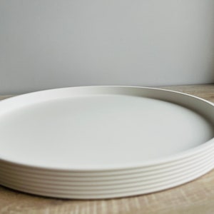 Könnte beinhalten: Ein weißes rundes Tablett aus übereinander gestapelten Tellern. Das Tablett ist leer und bereit für den Gebrauch.