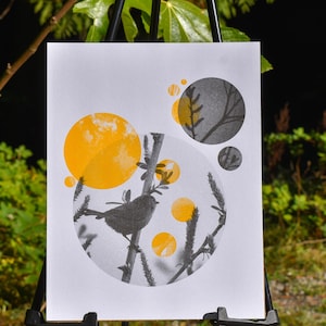 May include: A white art print featuring a black and white photograph of a bird perched on a branch within a large circle. The composition includes several solid yellow circles of varying sizes layered over the monochrome imagery.