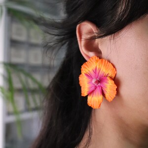 K&ouml;nnte beinhalten: Ein Paar orangefarbene und rosafarbene Ohrringe in Blumenform. Die Ohrringe sind aus einem weichen, biegsamen Material gefertigt und haben ein realistisches Blumendesign.