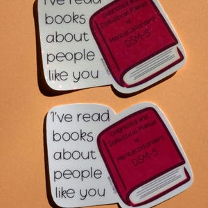 May include: Two stickers with the text "I've read books about people like you" and a red book that says "Diagnosed and Statistical Manual of Mental Disorders DSM-5". The stickers are on an orange background.