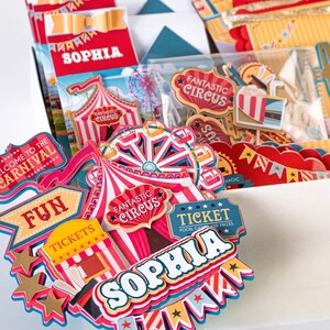 May include: A set of colorful carnival-themed party decorations with the name "Sophia" on a red and white striped tent, a ticket booth, and a Ferris wheel. The decorations are perfect for a birthday party or other celebration.