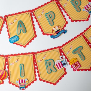 May include: A colorful banner with scalloped edges and red trim reads "Happy Birthday". Each letter is a different color and has a circus theme. The banner is decorated with small circus-themed images, including a ticket, popcorn, and a hot air balloon.