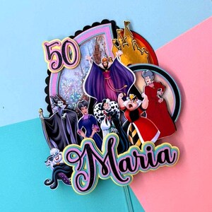 May include: A colorful cake topper featuring Disney villains, the number 50, and the name "Maria." The design includes images of a castle and various characters in vibrant colors. The background is a mix of pink and blue.